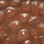 Brown milk chocolate bar with whole hazelnuts background.